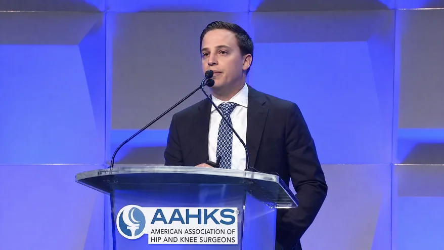 Dr. Grosso speaking at the podium of the American Association of Hip and Knee Surgeons annual meeting.