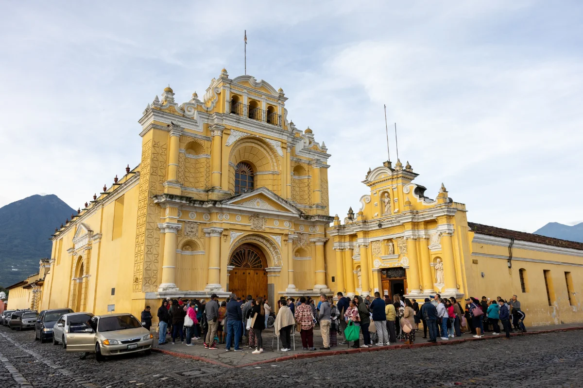 A crowd gathered outside a yellow colonial church in Antigua, Guatemala.
