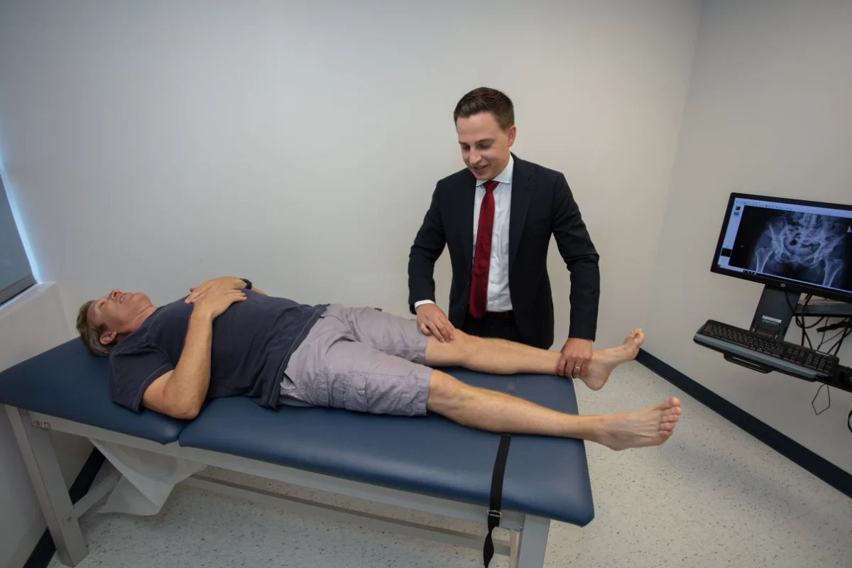 Dr. Grosso examining a patient’s hip on an exam table.
