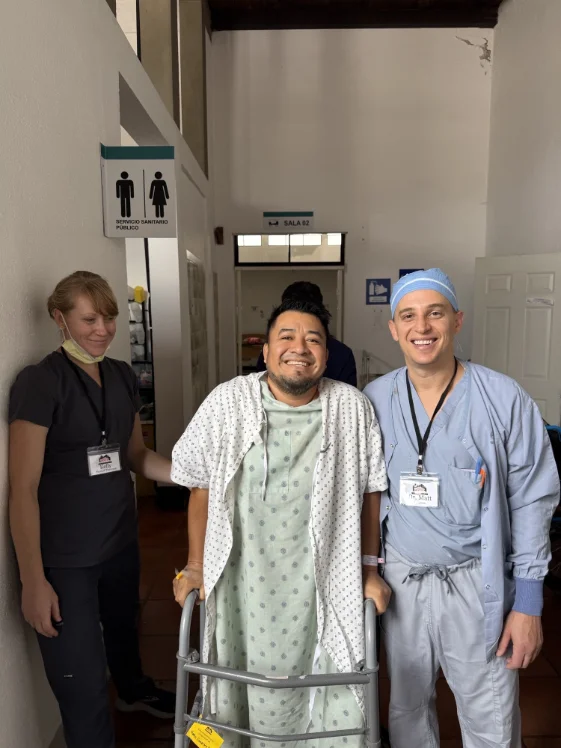 A patient standing with a walker after surgery, with Dr. Grosso and a team member at his side.