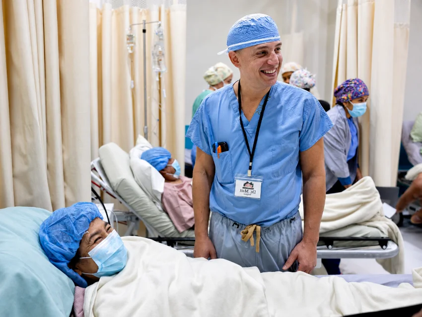 Dr. Grosso in scrubs at a patient’s bedside on the ward, both smiling.